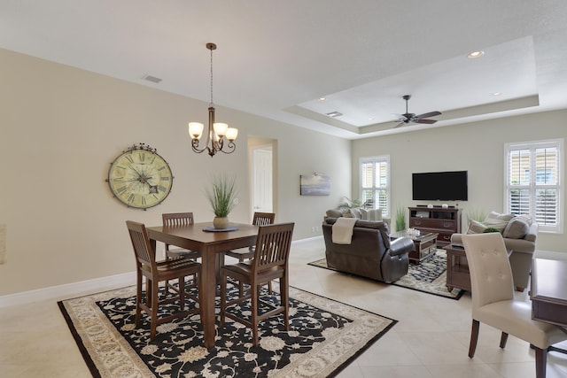 tiled dining area featuring ceiling fan with notable chandelier and a raised ceiling