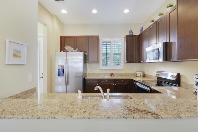 kitchen featuring a peninsula, appliances with stainless steel finishes, a sink, and light stone counters