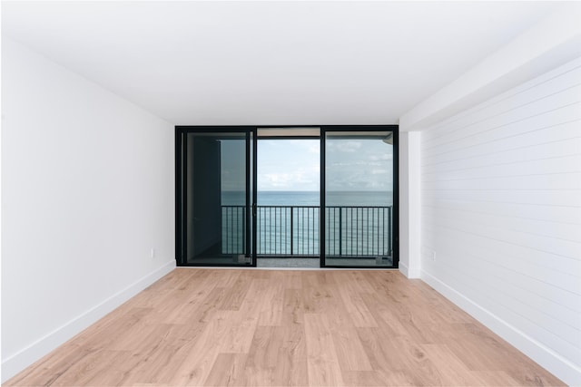 spare room with a water view, light hardwood / wood-style flooring, and a wall of windows