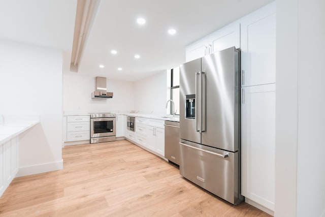 kitchen with white cabinets, wall chimney range hood, light stone countertops, appliances with stainless steel finishes, and light hardwood / wood-style floors