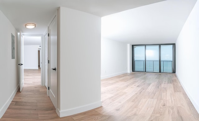 corridor with expansive windows, light hardwood / wood-style floors, and electric panel