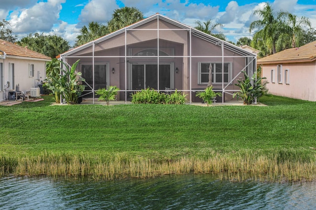 rear view of house featuring a water view, glass enclosure, and a lawn