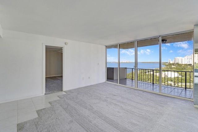 tiled empty room with a water view, a wall of windows, and carpet flooring