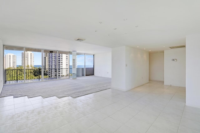 unfurnished room with plenty of natural light, light colored carpet, visible vents, and floor to ceiling windows