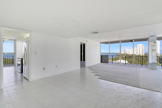 spare room featuring floor to ceiling windows, light tile patterned flooring, visible vents, and light colored carpet