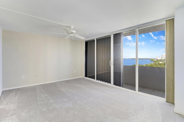 spare room with carpet floors, a water view, baseboards, and a ceiling fan