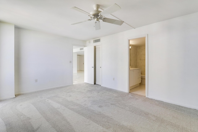 unfurnished bedroom featuring ensuite bath, visible vents, ceiling fan, and light colored carpet