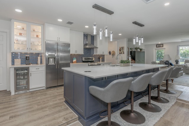 kitchen featuring white cabinets, stainless steel appliances, beverage cooler, and wall chimney range hood