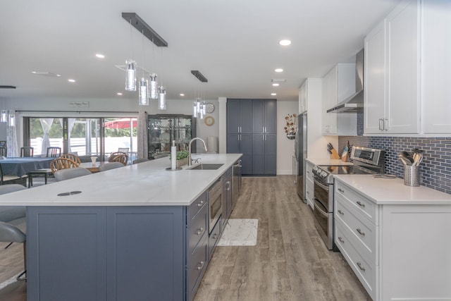 kitchen featuring sink, stainless steel appliances, wall chimney range hood, decorative light fixtures, and white cabinets