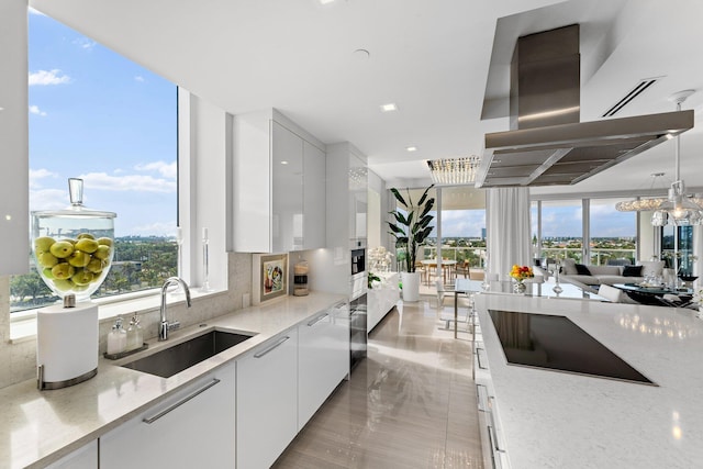 kitchen with sink, white cabinets, light stone countertops, and wall chimney range hood