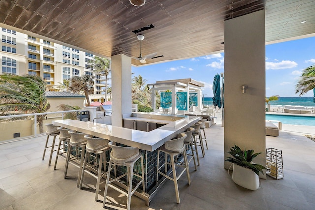 view of patio featuring a community pool, a water view, ceiling fan, and exterior bar