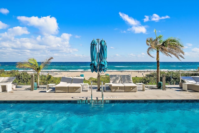 view of swimming pool with a beach view, a water view, and a patio