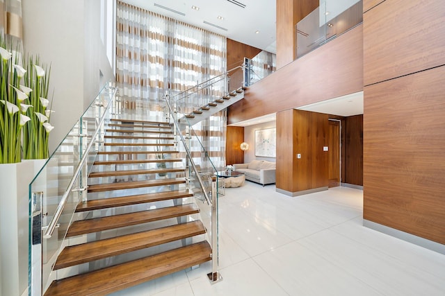 staircase with a towering ceiling, wood walls, and tile patterned floors