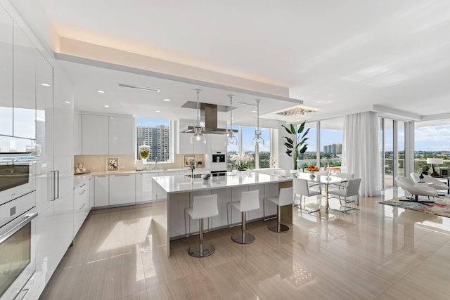 kitchen featuring white cabinetry, light tile patterned floors, oven, a kitchen island, and island range hood