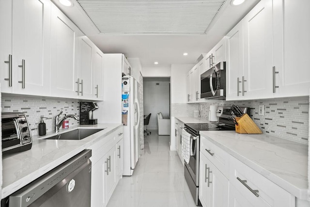 kitchen with light stone countertops, stainless steel appliances, white cabinetry, and sink