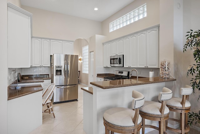 kitchen with kitchen peninsula, white cabinets, light tile patterned floors, and appliances with stainless steel finishes