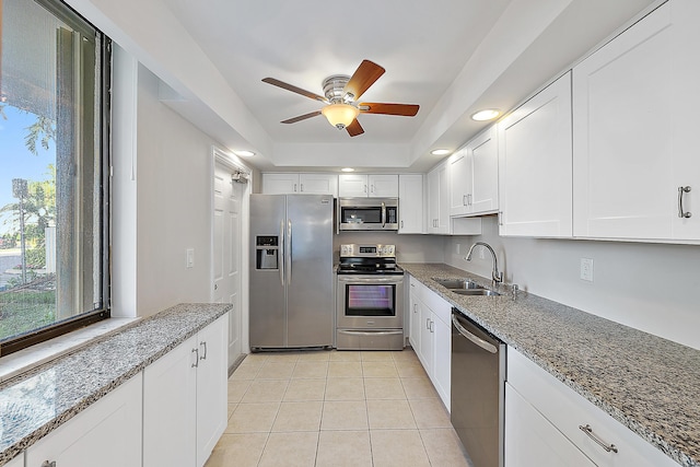 kitchen featuring light tile patterned floors, appliances with stainless steel finishes, dark stone countertops, white cabinetry, and a sink