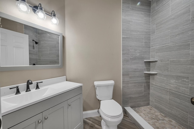 bathroom featuring tiled shower, vanity, hardwood / wood-style flooring, and toilet