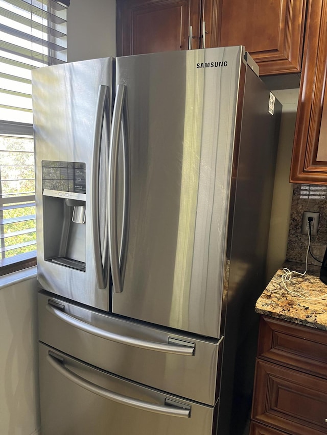 kitchen with light stone counters, backsplash, and stainless steel fridge with ice dispenser