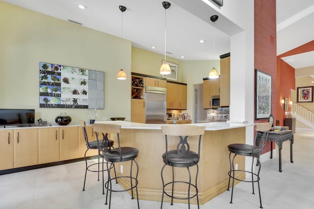 kitchen featuring hanging light fixtures, a high ceiling, a kitchen bar, light brown cabinetry, and appliances with stainless steel finishes