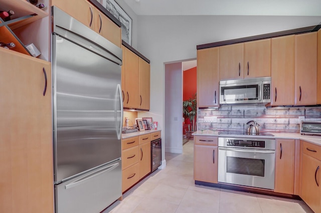 kitchen featuring light brown cabinets, backsplash, stainless steel appliances, and vaulted ceiling