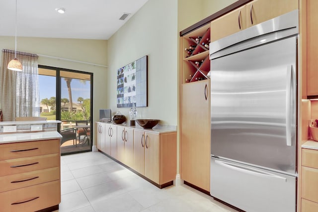 kitchen with vaulted ceiling, pendant lighting, light brown cabinets, light tile patterned floors, and stainless steel built in fridge