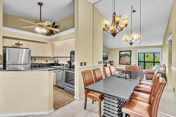 kitchen featuring ornamental molding, ceiling fan with notable chandelier, stainless steel appliances, cream cabinets, and pendant lighting