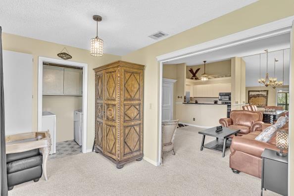 living room featuring a textured ceiling, washer and dryer, light colored carpet, and ceiling fan with notable chandelier