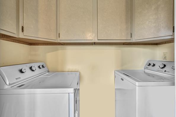 clothes washing area with cabinets and washing machine and clothes dryer