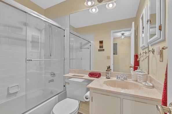 full bathroom featuring combined bath / shower with glass door, vanity, electric panel, and toilet