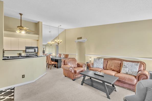 living room with light carpet, ceiling fan with notable chandelier, and vaulted ceiling