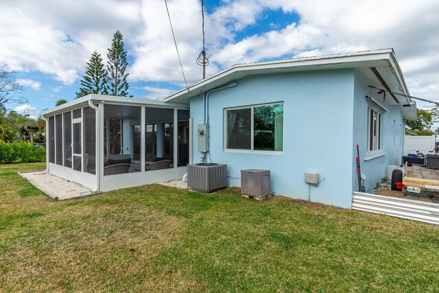 rear view of property with central AC, a sunroom, and a lawn