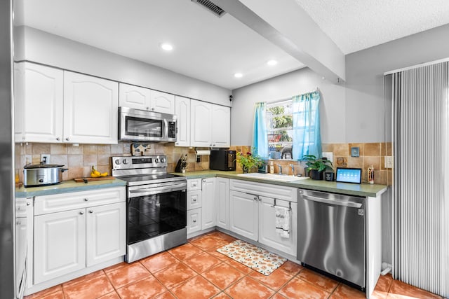 kitchen featuring decorative backsplash, stainless steel appliances, sink, light tile patterned floors, and white cabinets