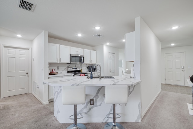 kitchen featuring white cabinetry, stainless steel appliances, light carpet, and a breakfast bar area