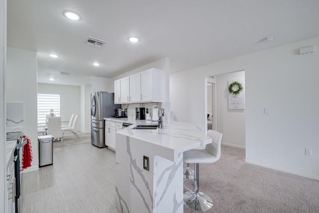 kitchen featuring sink, white cabinetry, appliances with stainless steel finishes, a kitchen breakfast bar, and kitchen peninsula