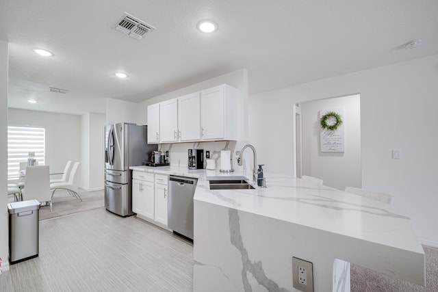 kitchen featuring sink, stainless steel appliances, light stone countertops, white cabinets, and kitchen peninsula