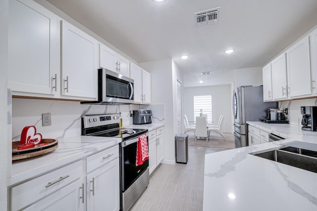 kitchen featuring light stone countertops, stainless steel appliances, white cabinets, and light wood-type flooring