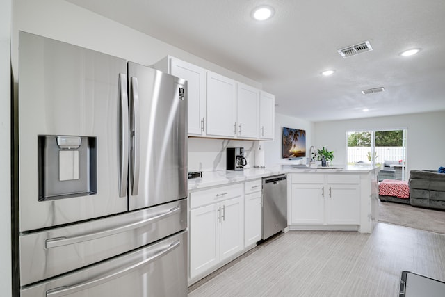 kitchen with appliances with stainless steel finishes, kitchen peninsula, sink, and white cabinets