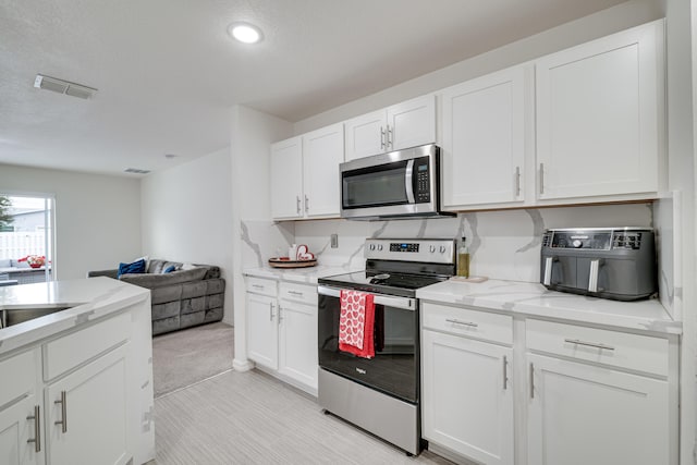 kitchen featuring light stone countertops, a textured ceiling, stainless steel appliances, and white cabinets