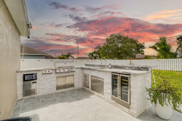 patio terrace at dusk with sink, a grill, cooling unit, wine cooler, and exterior kitchen