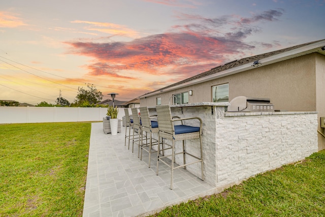 patio terrace at dusk with exterior kitchen, a yard, and a bar