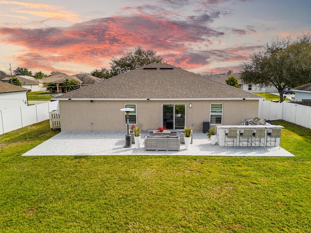 back house at dusk with a yard, exterior bar, and a patio