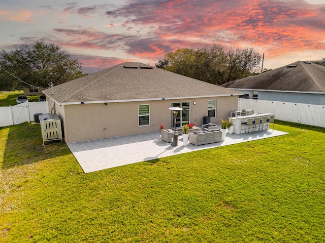 back house at dusk featuring a yard, outdoor lounge area, and a patio