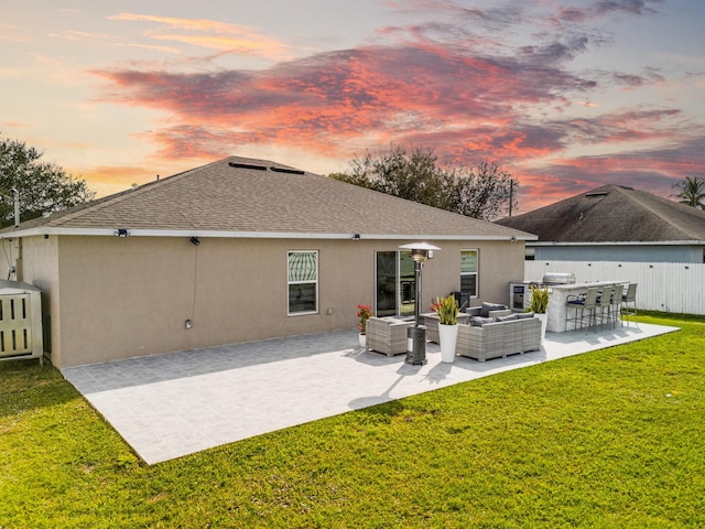 back house at dusk featuring an outdoor living space, exterior bar, a yard, and a patio area