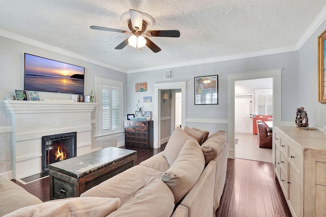 living room featuring ornamental molding, a textured ceiling, ceiling fan, dark wood-type flooring, and a fireplace