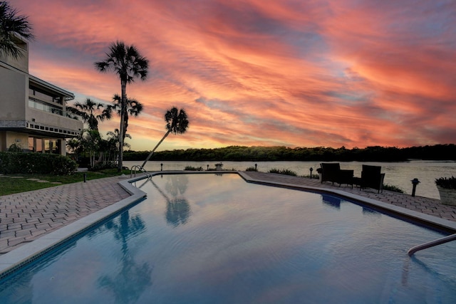 pool at dusk with a water view and a patio