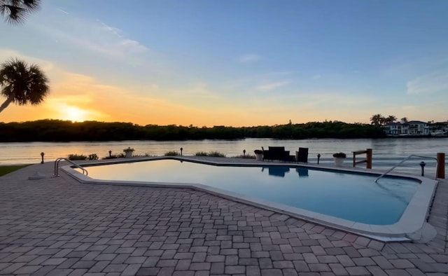 pool at dusk with a water view and a patio