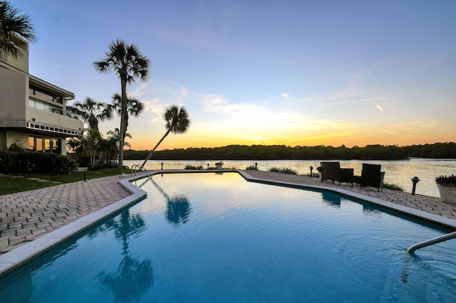 pool at dusk with a patio and a water view