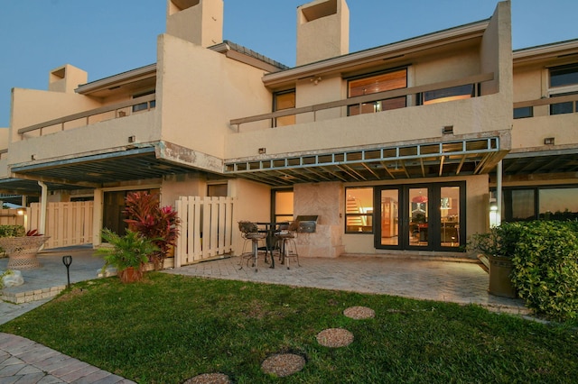 rear view of property featuring french doors, a balcony, a patio area, and a lawn