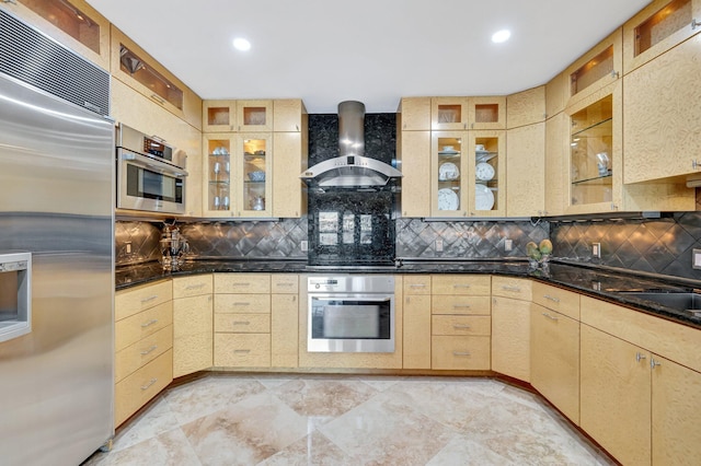 kitchen featuring tasteful backsplash, appliances with stainless steel finishes, wall chimney range hood, and light brown cabinetry